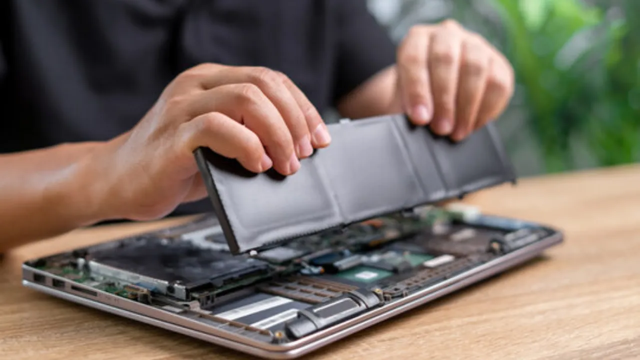 A person removing laptop battery from laptop.